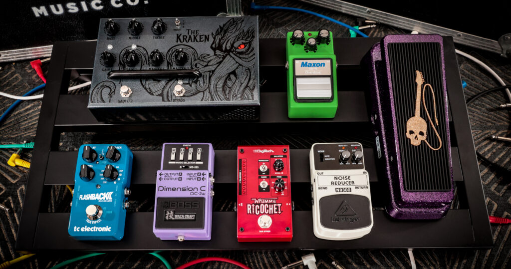 Deretan distortion pedal metal di atas papan pedal gitar dengan kabel terhubung